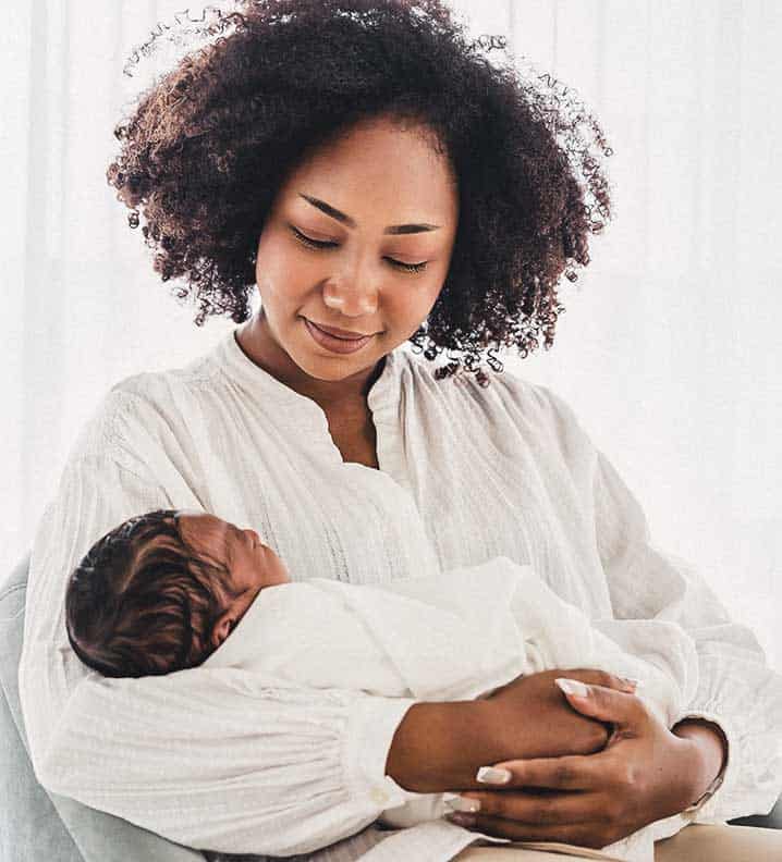 Household Staffing Newborn Care - A newborn care specialist smiles lovingly at a newborn baby